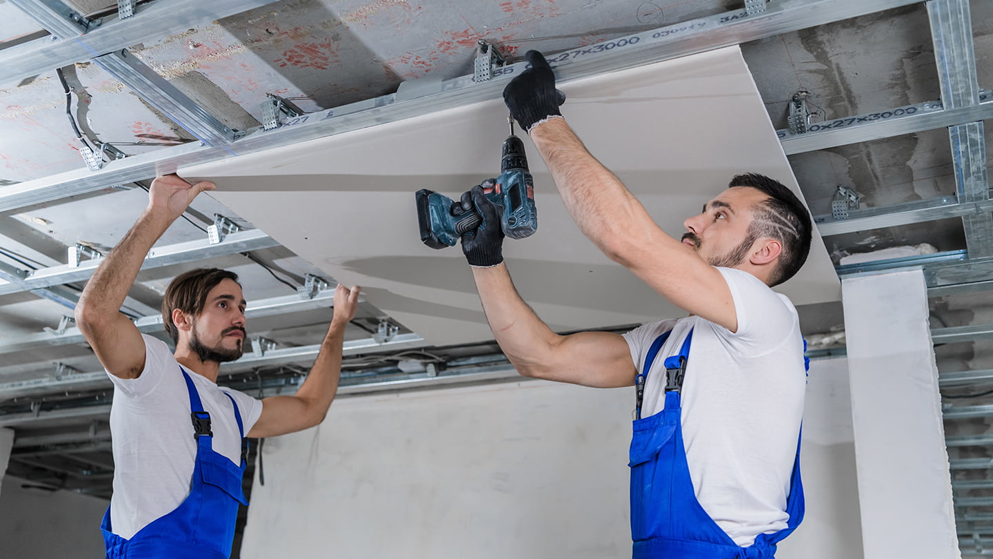 Zwei Handwerker montieren eine Gipskartonplatte an der Decke.